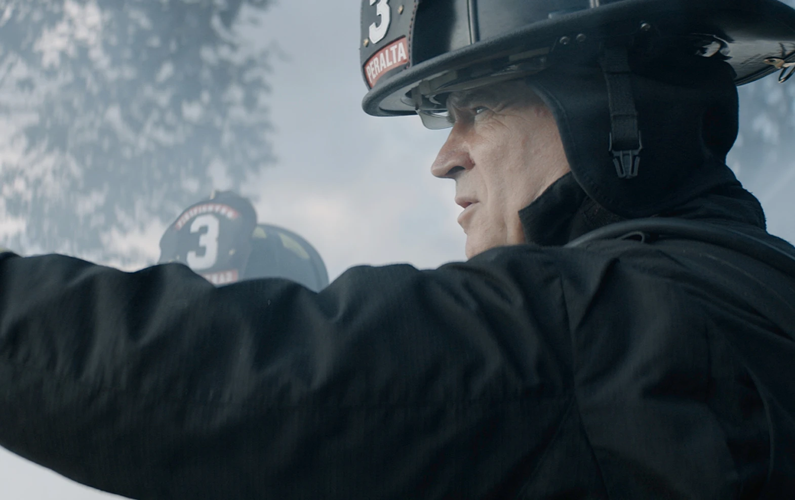 Side view of a firefighter in black gear and helmet numbered 3, looking intently forward and pointing.