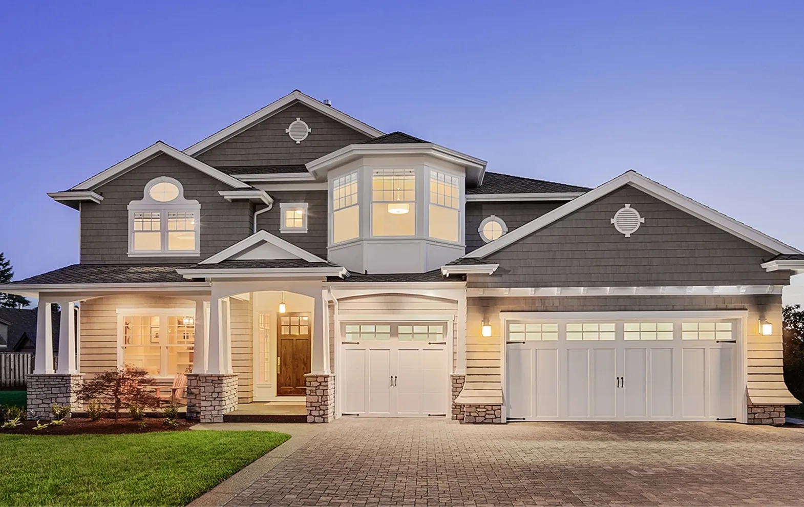 Two-story modern house with gray siding, white trim, bay window, and a three-car garage at dusk.
